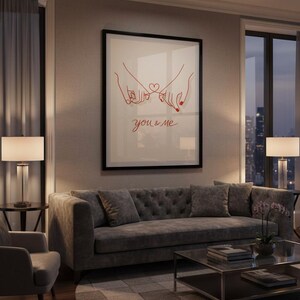 Puede incluir: Una impresi&oacute;n art&iacute;stica enmarcada con un dibujo lineal rojo de dos manos entrelazadas por los me&ntilde;iques, con un coraz&oacute;n y la frase "you & me". La obra de arte cuelga sobre un sof&aacute; gris en un sal&oacute;n moderno.
