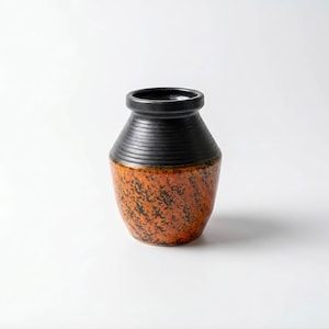 May include: A ceramic vase with a black rim and a textured, orange and black speckled body. The vase has a cylindrical shape with a slightly wider base and a narrower neck. The black rim has horizontal ridges.