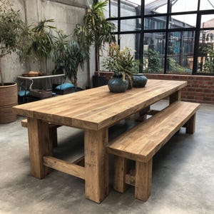 Puede incluir: Una mesa de comedor rectangular de madera grande con un banco a juego. La mesa y el banco son de madera de color marrón claro y tienen un estilo rústico y de granja. La mesa está sostenida por gruesas patas cuadradas. Dos jarrones azules con flores están sobre la mesa.