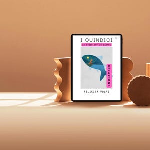 May include: A digital tablet displays a book cover with the title "I Quindici" and a blue fish illustration. The cover also includes the text "15 sfide per 15 giorni" and "Relazioni". The background is a warm, neutral color.