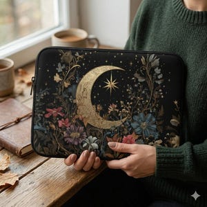 Könnte beinhalten: Schwarze Laptoptasche mit einem goldenen Halbmond- und Sterndesign, umgeben von floralen und botanischen Illustrationen in Rosa, Blau und Grün. Die Hülle hat einen schwarzen Reißverschluss und wird von einer Person gehalten.