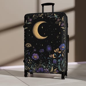 May include: A black rolling suitcase featuring a celestial design. The artwork includes a crescent moon, stars, and colorful flowers. The suitcase has a telescoping handle and four wheels for easy transport.