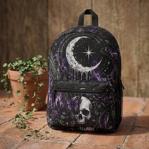 May include: A black backpack featuring a graphic print of a white crescent moon, a bright star, a human skull, purple butterflies, and dark floral elements. The bag includes a top handle, adjustable shoulder straps, and a front zippered pocket.