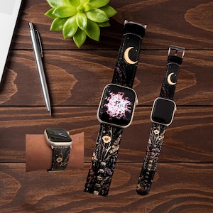 May include: Black watch bands with a floral and moon design. The bands feature a gold buckle and a black background with a pattern of flowers and a crescent moon. One watch is shown on a wrist.