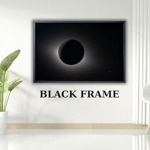 May include: A framed print featuring a black and white image of a solar eclipse. The artwork has a black frame and is mounted on a white wall. The text "BLACK FRAME" is printed below the image.