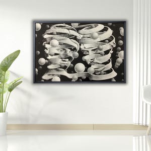 Può includere: Opera d'arte incorniciata in bianco e nero con due volti con elementi a nastro a spirale. Forme sferiche sono sparse intorno ai volti. L'opera è esposta su una parete bianca, con una pianta e una sedia in primo piano.
