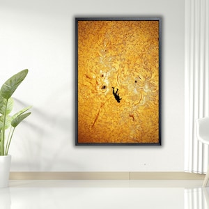 Op de afbeelding: Een ingelijste abstracte kunstprint met een zwarte rand. Het kunstwerk heeft een getextureerde, goudgele achtergrond met een donker silhouet van een figuur. De print wordt weergegeven in een modern, minimalistisch interieur.