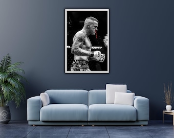 May include: Black and white framed print of a boxer in a UFC match. The boxer has blood on his face and is wearing gloves with the UFC logo. The image is displayed on a dark blue wall above a light blue sofa.
