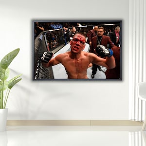 Può includere: Immagine incorniciata di un combattente di arti marziali miste in un incontro UFC. Il combattente è a torso nudo, con sangue sul viso e sul petto. Indossa guanti neri con il logo UFC. Lo sfondo mostra la gabbia e gli spettatori.