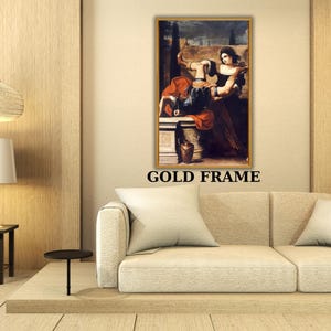 May include: A framed painting with a gold frame hangs above a beige sofa. The painting depicts two figures in classical attire. The text "GOLD FRAME" is printed in black below the painting. A lamp and side table are to the left.