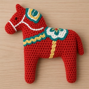 Może przedstawiać: Ręcznie robiony, czerwony koń z szydełka z białymi, żółtymi i turkusowymi akcentami. Ozdobny koń ma siodło i uzdę. Koń jest tradycyjnym przedmiotem sztuki ludowej, idealnym do dekoracji domu lub jako wyjątkowy prezent.