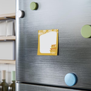 May include: A mustard yellow magnet with a white floral design and a blank white space for notes. The magnet features a stack of decorative bowls in a retro style. The magnet is attached to a stainless steel fridge door.