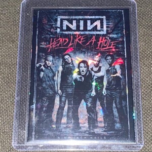 May include: A trading card featuring the band Nine Inch Nails. The card has the band's logo at the top, with the words "HEAD LIKE A HOLE" in red. The band members are in the center, with a dark background.