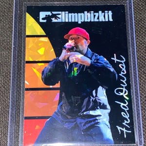 May include: A trading card featuring Fred Durst of Limp Bizkit. The card shows Durst in a red cap and black jacket, holding a microphone. The Limp Bizkit logo is at the top, with "Fred Durst" in cursive on the right.