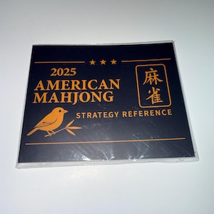 May include: A black and gold strategy reference card for American Mahjong. The card features the text "2025 AMERICAN MAHJONG" and "STRATEGY REFERENCE". A gold bird illustration is on the bottom left.