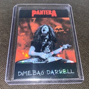 May include: A Pantera trading card featuring Dimebag Darrell playing guitar. The card has a red and orange background with skulls. The band's name, "PANTERA", is at the top. The text "DIMEBAG DARRELL" is at the bottom.