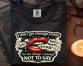 Può includere: T-shirt nero girocollo con grafica di labbra rosse e la scritta "I don't get enough credit for the things I manage NOT TO SAY." La maglietta ha un'etichetta Comfort Colors.