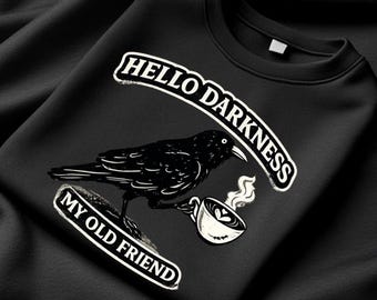 Può includere: Felpa nera con grafica di un corvo che tiene una tazza di caffè. Il testo "HELLO DARKNESS MY OLD FRIEND" è arcuato sopra e sotto il corvo. Il design è in bianco.