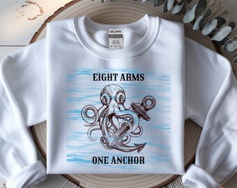 Può includere: Felpa bianca con grafica di un polpo che tiene un'ancora. Il testo "EIGHT ARMS ONE ANCHOR" è sopra e sotto l'illustrazione. Il design presenta linee d'acqua blu e un tema nautico.
