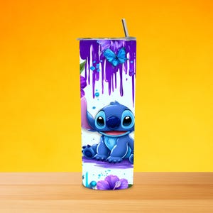 K&ouml;nnte beinhalten: Ein zylindrischer Edelstahlbecher mit einer blauen Alien-Figur, violetten Farbtropfen-Mustern und leuchtend blauen Schmetterlingsillustrationen. Das Design zeigt violette Hibiskusbl&uuml;ten auf wei&szlig;em Hintergrund mit einem Metallstrohhalm.