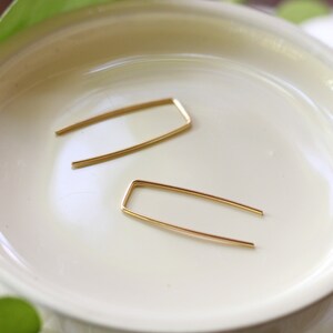 May include: A pair of gold-toned, open rectangle shaped earrings. The earrings are laying on a white surface.