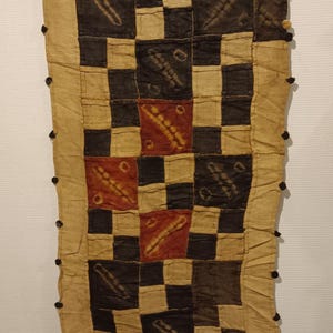 Può includere: Tessuto rettangolare con un motivo a scacchi beige, nero e rosso. Il tessuto sembra fatto a mano, con cuciture visibili e un bordo sfrangiato. Il design presenta forme geometriche e motivi astratti.