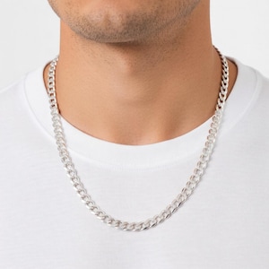 May include: A silver curb chain necklace. The necklace is made of interlocking links and is worn around the neck. The person is wearing a white t-shirt.