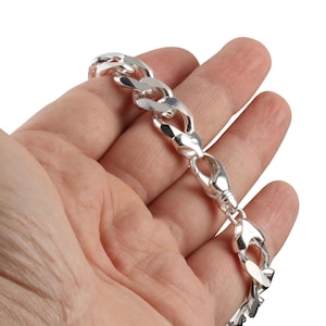 May include: A silver chain bracelet with a large link design. The bracelet is made of a shiny, reflective metal and features a lobster clasp closure. The bracelet is held in a person's hand.