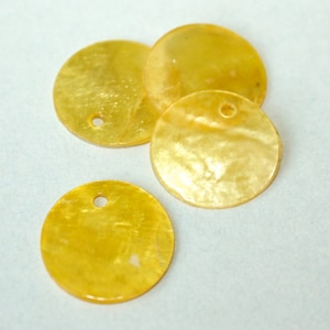 May include: Four round, golden-yellow shell beads with a pearlescent sheen. Each bead has a small hole near the top for stringing. The beads are scattered on a light background, showcasing their natural color and texture.