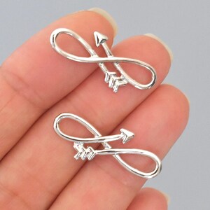 May include: Two silver-colored infinity symbol charms with arrows. The charms are in the shape of the infinity symbol, with an arrow piercing through the center. The arrows have a detailed feather design.