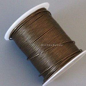 May include: A spool of bronze-colored cord wound around a white plastic core. The cord appears to be leather or a similar material, with a slightly textured surface. The spool is angled, showing the tightly packed coils.