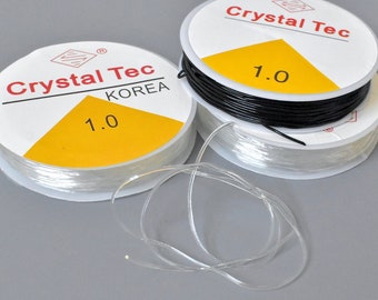 May include: Spools of clear and black elastic string, labeled "Crystal Tec KOREA 1.0". The clear string is unwound, showing its flexibility. The spools have a white label with red text and a yellow triangle.