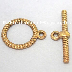May include: A gold-toned toggle clasp set featuring a circular ring and a T-bar component, both with a twisted rope texture. The ring has a small loop attachment, and the T-bar has a central loop. The text MichouBeads is visible.