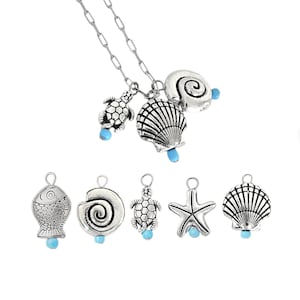 May include: A silver-toned necklace with a chain and several ocean-themed charms. Charms include a seashell, a snail shell, a turtle, and a starfish, each with a small blue bead. Additional charms of a fish, snail shell, turtle, starfish, and seashell are also shown.