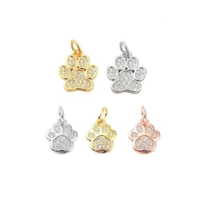 Puede incluir: Cinco dijes con forma de huella de pata con cristales transparentes. Los dijes son de oro, plata y oro rosa.