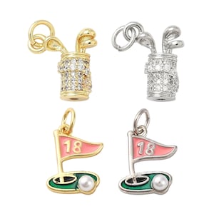 May include: Four golf-themed charms. Two charms feature golf clubs in a bag, one gold-toned and one silver-toned, both encrusted with clear stones. The other two charms are pink and green golf flags with the number 18 and a pearl.