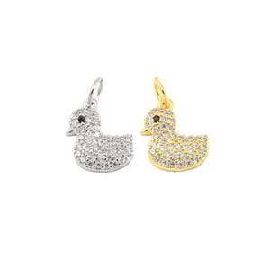 May include: Two duck-shaped pendants. One is silver-toned with clear stones, the other is gold-toned with clear stones. Both have a black stone for the eye and a loop for hanging.