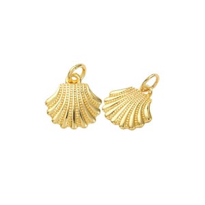 May include: Two gold-colored seashell charms with a textured surface and a loop for attaching to a necklace or bracelet. The charms are detailed with ridges and small dots, and are set against a white background.