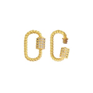 May include: Two gold-colored, oval-shaped clasps. Each clasp has a twisted rope design. One clasp is closed, and the other is open, with a cylindrical section covered in small, clear stones. The clasps are set against a white background.