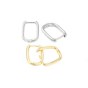 May include: Three pairs of hoop earrings in silver and gold. The earrings have a rectangular shape with a hinged closure. The earrings are displayed on a white background.
