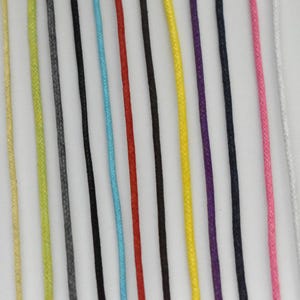 May include: A collection of twelve thin, braided cords arranged vertically in parallel lines. The colors include light yellow, lime green, gray, black, light blue, red, dark brown, bright yellow, purple, navy blue, pink, and white.