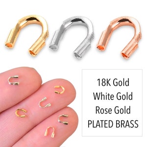 May include: Three gold-plated brass crimp end beads in gold, white gold, and rose gold. The beads are shown on a white background and on a person's fingers.