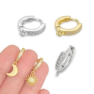 May include: A pair of hoop earrings with a dangling charm. One earring has a gold hoop with a sun charm and the other earring has a silver hoop with a moon charm. Both hoops are decorated with small clear cubic zirconia stones.