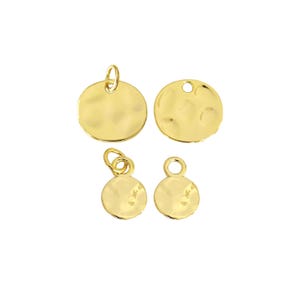May include: Four gold-colored hammered disc charms. Two larger charms have a loop at the top, and two smaller charms have a loop at the top. The charms are round with a textured surface.