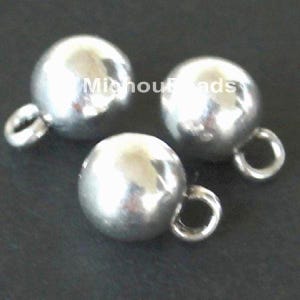 May include: Three polished silver-toned spherical beads, each featuring a small circular loop attached to the side for hanging. The smooth, reflective surface of the metal spheres catches the light, creating bright highlights on the round shapes.