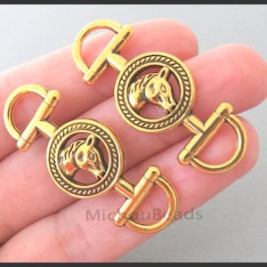 May include: Two gold-toned metal connectors featuring a circular center with a raised horse head design surrounded by a rope-like border. Each connector has a semi-circular loop on both ends, creating a classic equestrian-inspired hardware piece.