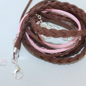 Pu&ograve; includere: Un cordoncino in pelle intrecciata marrone e rosa con una chiusura argentata. Il cordoncino &egrave; composto da pi&ugrave; fili di pelle intrecciati insieme. Il cordoncino &egrave; lungo circa 25 cm e ha una chiusura argentata a un'estremit&agrave;.