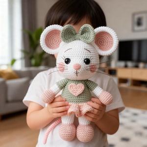 K&ouml;nnte beinhalten: Handgefertigte H&auml;kelmaus-Puppe mit wei&szlig;em K&ouml;rper, rosa und wei&szlig;en Ohren und einer gr&uuml;nen Schleife. Die Maus tr&auml;gt ein gr&uuml;nes Shirt mit einem rosa Herz und einen rosa Rock. Die Puppe ist etwa 25 cm gro&szlig;.