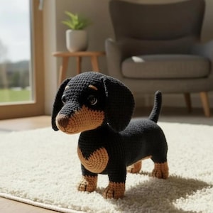 Puede incluir: Un perro salchicha de ganchillo en negro y marrón claro. El juguete de peluche hecho a mano tiene orejas grandes y caídas, un cuerpo largo y patas cortas. El perro está de pie sobre una alfombra color crema.