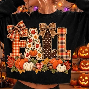 Può includere: Una felpa nera a maniche lunghe con la scritta FALL in grandi lettere stampatello. Ogni lettera presenta un motivo unico tra cui tartan arancione, foglie autunnali, pois marroni e tartan rosso, decorata con fiocchi e zucche.